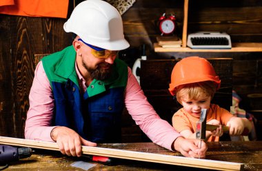 Babam oğluna tahta atölyede çekiç ve çivi kullanarak nasıl diy yapılacağını gösteriyor. Baba ve oğul marangoz aletleri kullanıyor. Küçük İnşaatçı