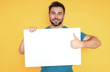 Stüdyo arka planında boş afişi olan bir adam. Elinde boş bir poster tutan adamın portresi. Boş afiş gösteren bir adam işaret ediyor. Erkek panosu, reklam panosu ya da panosu