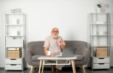 Yetişkin bir adam iş eğitimini izliyor, dizüstü bilgisayarda internetten giyiniyor, uzaktan kumandayla çalışıyor. Video konferansında yaşlı işadamı sanal sohbet çağrısı yapıyor