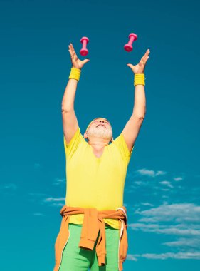 Mavi arka planda izole edilmiş dambıllı kıdemli fitness adamı eğitimi. Yaş, sağlığını kaybetmen için bir bahane değil.