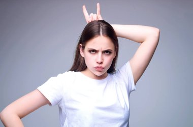 Parmakları boynuzlu ve kızgın yüzlü bir kadın. Öfkeli, nefret dolu, öfkeli kız. Öfkeli kadın suratı. Öfkeli, negatif duygu portresi olan bir kadın. Saldırgan ve deli kız stüdyoda kötü davranışlar sergiliyor.