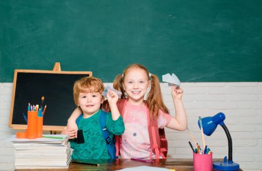 Okula geri dön - eğitim konsepti. Kağıt uçaklı çocuklar. Okul malzemeleri ile masa nın yanında mutlu yüz ifadesi ile kız ve erkek