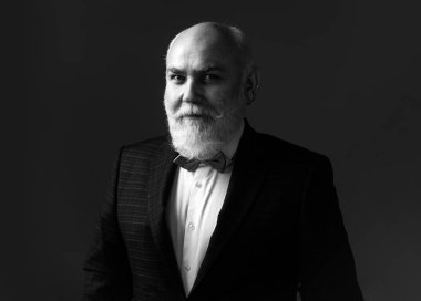 Takım elbiseli ve kravatlı kendinden emin yaşlı sakallı adam gri izole arka planda duruyor. Moda kıyafetli yetişkin adam pozu