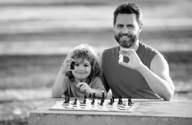 Dışarıda mutlu bir aile. Çocuk satranç oynuyor. Baba oğul bahar bahçesinde satranç oynuyorlar.