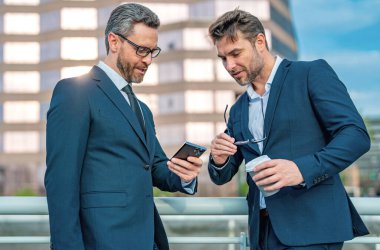 Şehirdeki arka planda çalışan beyaz bir çalışan cep telefonundan mesaj yolluyor. Açık havada akıllı telefon kullanan resmi takım elbiseli bir iş adamı.