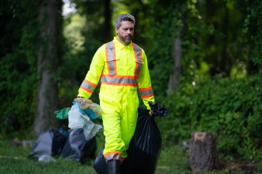 Gönüllü adam çöpleri topluyor, doğadaki atıkları topluyor. Toprak kirliliği, çevresel sorunlar. Plastik çöp yığını doldur. Doğanın kirliliği. Ekoloji konsepti. Çevre kirliliği