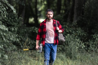 Oduncu balta tutuyor. Ormanda ciddi bir yüzü var. Büyük baltalı bir oduncu kesmeden önce ağacı inceler. Ciddi bir oduncu. Kendine güvenen genç sakallı adam elinde büyük bir balta tutuyor.