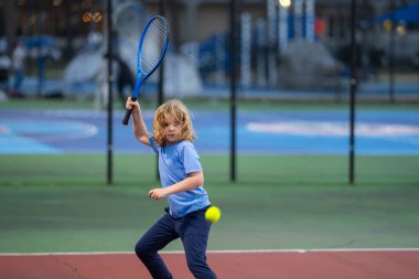 Şirin Çocuk tenis oynuyor. Küçük çocuk tenis raketiyle tenis topuna vurdu. Çocuklar için aktif egzersiz. Çocuklar için yaz etkinlikleri. Çocuk tenis oynamayı öğreniyor. Sport Kid sahada topa vuruyor.