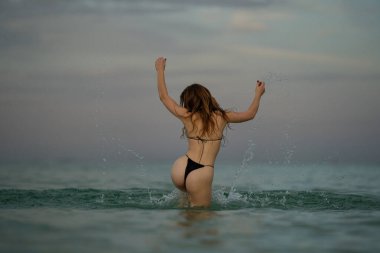 Sexy bikini booty woman playful on paradise tropical beach. Young woman with sexy buttocks ass butt splashing in sea water. Beautiful fit body girl on luxury summer travel vacation