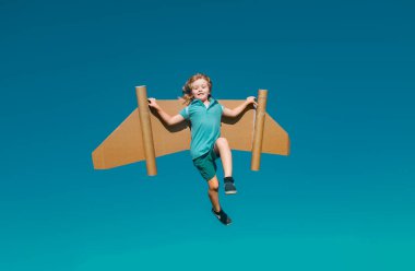 Mavi gökyüzüne karşı kağıt kanatlı mutlu çocuk. Oyuncak sırt roketli çocuk yeşil baharda dışarıda eğleniyor. Özgürlük tasasız ve çocukların hayal gücü kavramı