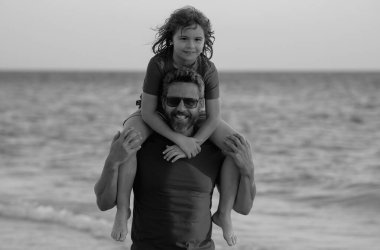 Oğullar babalarının omuzlarına biner. Baba ve oğlu o gün kumsalda yürüyorlardı. Mutlu bir aile. Babalar Günü. Oğullar babalarının omuzlarına biner. Ebeveynlik, babalık, babaların sevgisi.