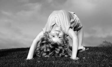 Çocuk yaz parkında yeşil çimlerin üzerinde baş aşağı duruyor. Sağlıklı aile hayatı kavramı. Eğlenceli ve tasasız bir çocukluk. Çocuk egsersiz yapıyor.