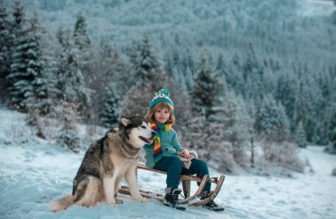 Küçük çocuk köpeğe sarılıyor ve karda eğleniyor. Kış gezgini çocuk