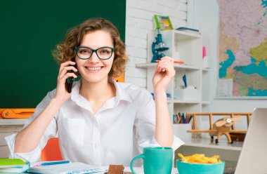 Sınıfta karatahtanın üzerinde cep telefonu olan bayan öğretmen. Sınıftaki üniversiteli kız