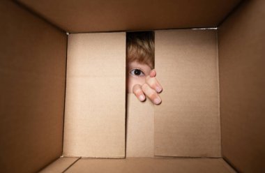 Amazed adorable little boy peeking inside gift box, unpacking present with funny astonished expression, impatient child unboxing surprise. Close up eyes looking