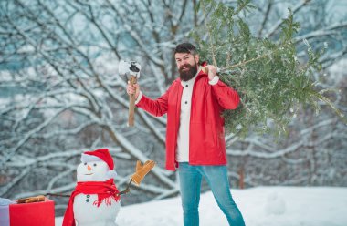 Baltalı Noel oduncusu ve Noel ağacı. Sakallı Adam Noel ağacını kesiyor. Kış ormanında baltayla oduncu. Genç oduncu ormandaki Noel ağacını kesiyor.