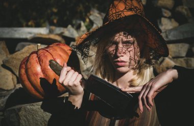 Kabak ile ahşap arka plan üzerinde poz cadı. Mutlu Gotik genç kadın cadı halloween kılık. Cadılar Bayramı kavramı. Kabak ile poz cadı. Gotik kadın cadı halloween kılık şapka ile
