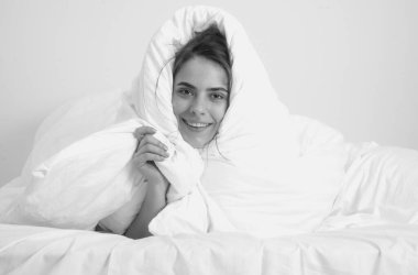 Beautiful young woman covered with warm blanket on bed at home