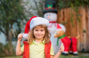 Mutlu yıllar ve mutlu Noeller. Noel Baba şapkalı komik çocuk evin arka bahçesini duyuyor. Noel akşamı