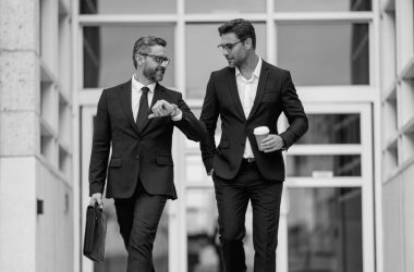 Takım elbiseli iki çekici, kendine güvenen İspanyol işadamı şehir sokaklarında yürüyor. Şehir merkezinde yürüyen ve konuşan iki işadamı. Orta Doğulu işadamı ofis binasının yakınında yürüyor