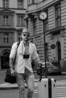Tatil için bavulu olan adam, yolculuk. Seyahat çantalı bir turist. İş gezisindeki yakışıklı genç adam bavuluyla sokakta yürüyor. Gezgin iş adamı.