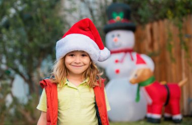 Mutlu yıllar ve mutlu Noeller. Noel Baba şapkalı çocuk evin arka bahçesini duyuyor. Noel akşamı