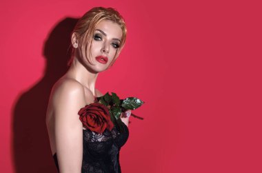 Kırmızı stüdyo arka planında izole edilmiş kırmızı güller tutan çekici, sevimli, hayalperest kızın portresi.