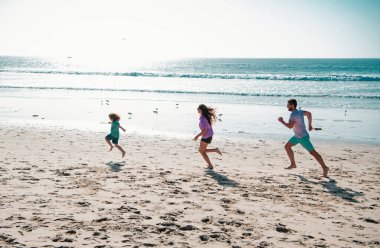 Mutlu genç aile yaz plajında koşup zıplıyor. Arkadaş canlısı aile kavramı ve yaz tatili. Ailesi koşan ve zıplayan çocuk