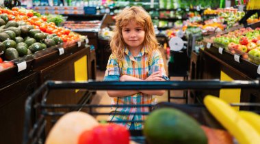 Süpermarkette meyve alan bir çocuk. Çocuk bakkal alışverişi. Alışveriş arabalı çocuk marketten taze sebze seçiyor. Alışveriş arabası, market konsepti.