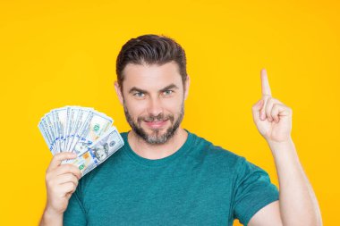 İyi ödeme. Yakışıklı adam gri stüdyoda izole edilmiş para tutuyor. Dolar banknotları halinde para. Yığınla para, finans, yatırım ve tasarruf