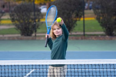 Tenis. Tenis raketi ve tenis topu olan çocuk tenis kortunda oynuyor.