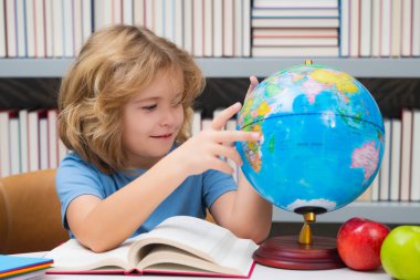 School boy looking at globe in library, geography lesson. School child student learning in class, study english language at school. Elementary school child. Portrait of funny pupil learning