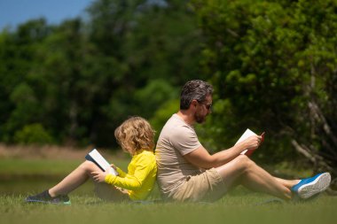 Baba ve oğul parkta kitap okuyor. Eğitim ve arkadaşlık kavramı. Hayat tarzı, babası sevimli oğluna bir kitap okumuş. Sıcak bir yaz günü, aile ilişkisi, çocuk ve ebeveyn, bekar.