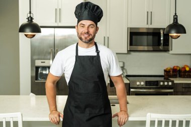 Üniformalı yakışıklı aşçı mutfakta yemek yapıyor. Restoran menüsü konsepti. Fırıncı üniformalı İspanyol adam. Aşçılık ve aşçılık. İş üniformalı, siyah önlüklü, şef şapkalı bir aşçı.