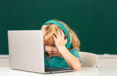 Kızgın üzgün çocuk kulaklık takıyor, sınıfta dizüstü bilgisayarla çalışıyor, müzik dersi dinliyor.