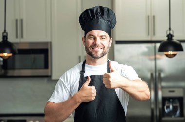 Mutlu aşçı baş parmağı yukarıda. Aşçı aşçı adam. Milenyum aşçı üniformalı erkek şef. Aşçı mutfakta yemek pişiriyor.