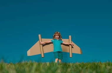 Child boy playing with cardboard toy airplane wings craft in sky with copy space for text. Creative with family and dreaming of flying concept. Travel and imagination concept