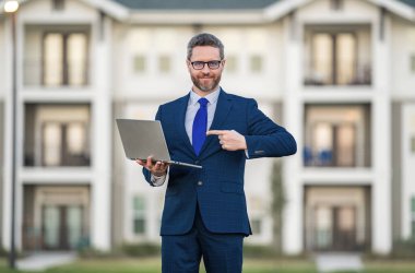 İş adamı dışarıda dizüstü bilgisayar kullanıyor. Erkek işadamı dizüstü bilgisayarı evin önünde tutuyor. Dizüstü bilgisayar kullanan bir adam. Beyaz tenli gözlüklü bir erkek bilgisayar ve açık hava portresi kullanıyor.