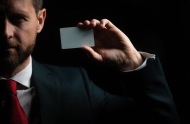 Siyah kostümlü ve kırmızı kravatlı bir işadamı kredi kartı ya da kartvizit gösteriyor. Kapatın. Elinde boş bir kredi kartı modeli var. Kredi kartı, kol tutma şablonu oluşturur