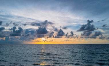 Gökyüzü ve bulutların arasından güneş batarken deniz batıyor. Okyanus ve gökyüzü arkaplanı, deniz manzarası.
