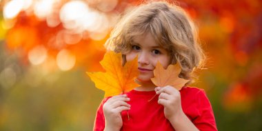 Sonbahar Çocuk Portresi ve Sonbahar Sarı Yaprakları. Autumn Park 'ın dışındaki güzel çocuk. Parkın dışındaki yaprakları tutan sevimli çocuk yüzünü kapat. Çocukluk, sonbahar ve eğlence. Sonbahar yeşilliği