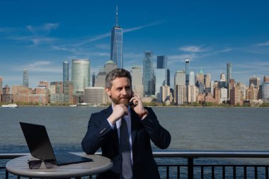 Zengin iş adamı, serbest çalışan. Takım elbiseli bir iş adamı New York 'ta dışarıda dizüstü bilgisayar kullanıyor. Amerikan işi. Manhattan yakınlarında takım elbiseli Amerikalı iş adamları. Açık hava işi. ABD 'de iş