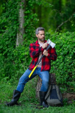 Erkek gücü. Kaslı seksi oduncu. Ağaç kesme konsepti. Ormanda kereste işçisi. Ormanda baltayla oduncu. Vahşi sakallı baltalı oduncu.