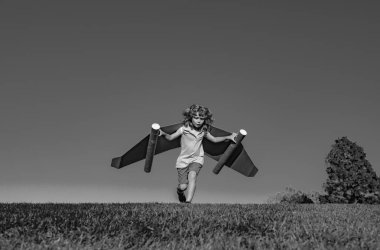 Child boy playing with cardboard toy airplane wings craft in sky with copy space for text. Creative with family and dreaming of flying concept. Travel and imagination concept