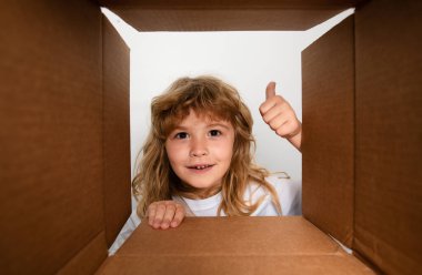 Başparmağı havada komik çocuk hediyesini açıyor ve karton kutunun içine bakıyor. Paketleme veya açma kavramı