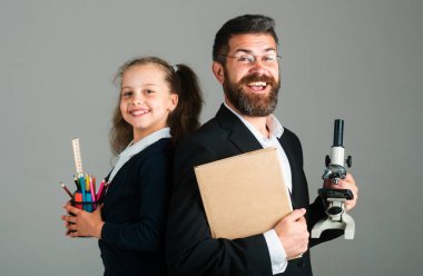 Heyecanlı, mutlu bir öğrenci kız öğrenci ile harika bir öğretmen. Komik öğrenci portresi ve okul malzemeleriyle özel öğretmen. Gri arka planda izole edilmiş mutlu öğretmen ve öğrenci kız. Okula geri dön.