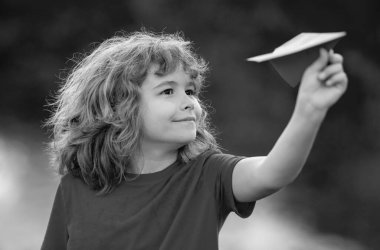 Mutlu çocuk kağıt uçak tutuyor. Oyuncak uçak çocukların elinde. Mutlu çocuk eğiliyor ve sarı kağıt uçak fırlatıyor. Çocuk kağıt uçakla oynuyor. Kağıt uçakla oynayan çocuk