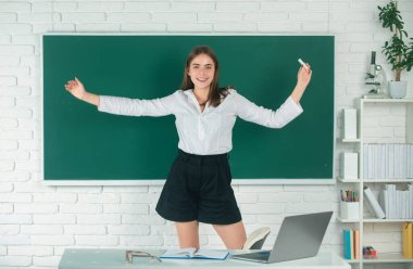 Kız öğrenci, lisede ya da üniversitede tebeşirle tebeşirle elini kaldırmış, heyecanlı amazet öğrencisini karatahta üzerine oturtmuş.
