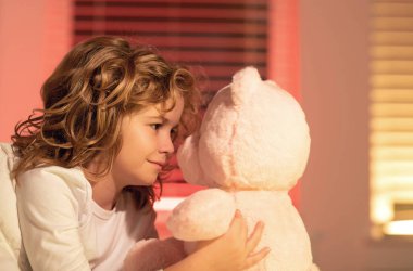 Oyuncak ayıyla oynayan bir çocuk. Yatağında oyuncak ayısı olan tatlı, uykulu bir çocuk, yatma zamanı, çocukluk dönemi ve büyüyen çocuklar konsepti, kapalı mekan portresi. Uykulu bir çocuk.