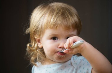 Kirli suratla bebek yemek. Neşeli, gülümseyen çocuk kendini kaşıkla yiyor. Bebek pis suratıyla yiyor. Mutfakta yemek yiyen gülümseyen küçük bir çocuk. Çocuk aç.